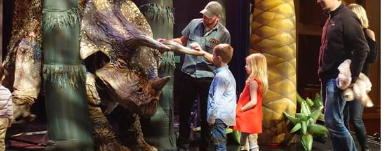 man showing a sculpture of a triceratops to two children