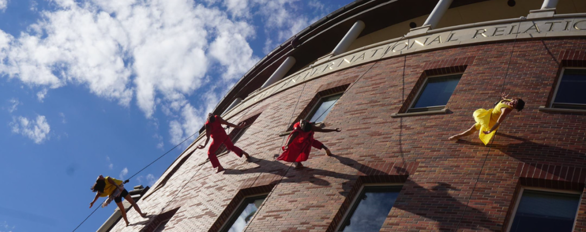 dancers hanging on ropes on building exterior