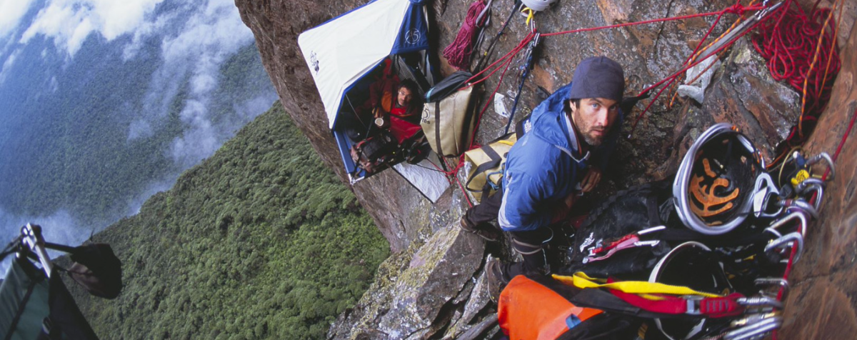 2 men with extensive climbing gear on rock wall